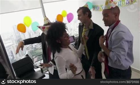 Business woman celebrating her birthday and doing a party with colleagues in her office. This group of friends and coworkers have fun dancing and smiling. Medium shot, slowmotion 120p