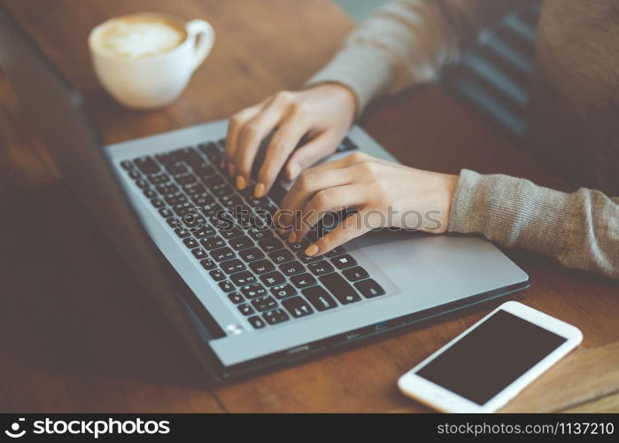 business woman freelance sitting using working on his computer notebook laptop and mobile smart phone send work with coffee cup on the table wooden in a cafe coffee shop. working women.