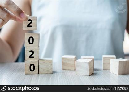 Business woman hand holding wooden cube with 2020 word on table background. Resolution, strategy, solution, goal, business, New Year New You and happy holiday concepts