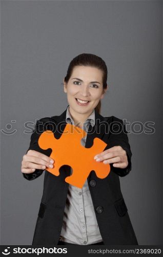 Business woman holding a big puzzle piece, over a gray background