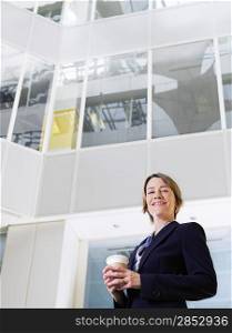 Business woman holding cup of coffee standing in atrium of office building low angle view