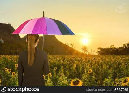 business woman holding multicolored umbrella in sunflower field and sun light