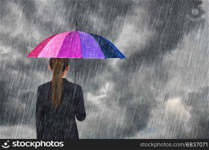 business woman holding multicolored umbrella under dark sky with falling rain