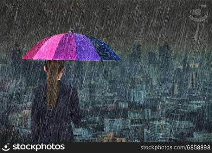 business woman holding multicolored umbrella with falling rain at Bangkok city background, Thailand