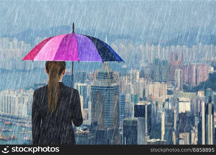 business woman holding multicolored umbrella with falling rain at city background