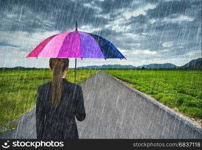 business woman holding multicolored umbrella with falling rain at country road