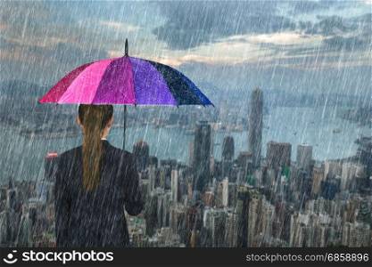 business woman holding multicolored umbrella with falling rain at Hong Kong city background