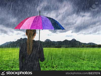 business woman holding multicolored umbrella with falling rain at Khao Jeen Lae, big mountain at Lopburi, Thailand