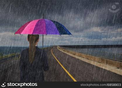 business woman holding multicolored umbrella with falling rain on the road