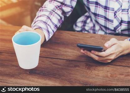 Business woman holding phone and coffee cup on wooden table. Vintage toned.
