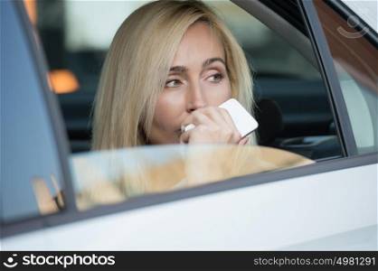 Business woman in a car looking away and holding smartphone