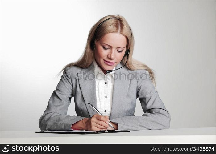 business woman in a headset writing in notebook