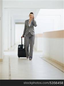 Business woman in business trip walking with wheel bag and speaking mobile
