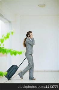 Business woman in business trip with wheel bag speaking mobile