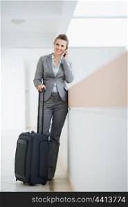 Business woman in business trip with wheel bag speaking mobile