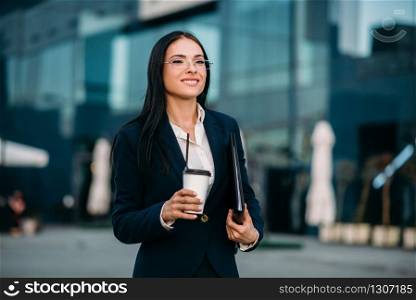 Business woman in glasses with coffee in hands, against skyscraper. Modern building, financial center, cityscape. Successful female businessperson. Business woman in glasses with coffee in hands