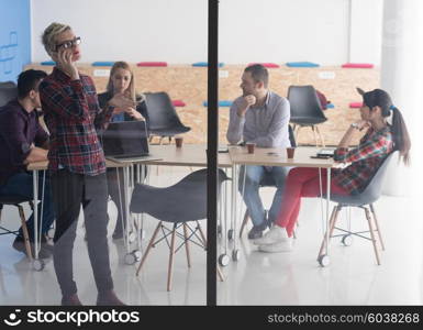 business woman in meeting room speaking by cell phone, people groupbrainstorming in background