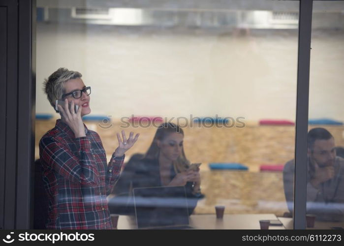 business woman in meeting room speaking by cell phone, people groupbrainstorming in background