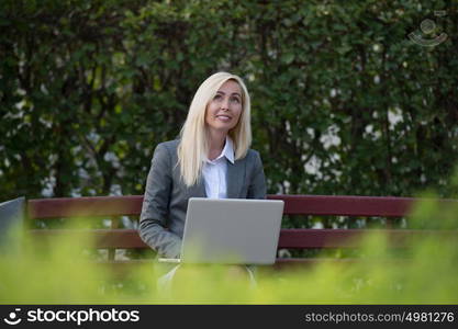 Business woman in park sitting on bench and using laptop