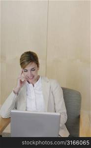 Business woman in tan jacket has hand next to her face as she looks down at her laptop