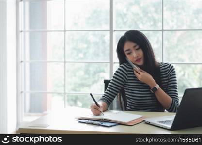 Business woman is busy,talking on smartphone, making notes and working on laptop.