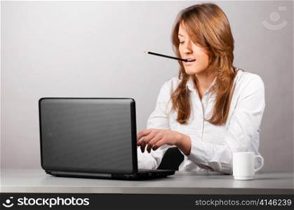 business woman is sitting in the office with laptop and working hard with pencil in her teeth