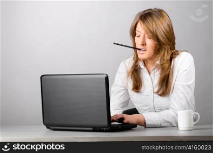 business woman is sitting in the office with laptop and working hard with pencil in her teeth
