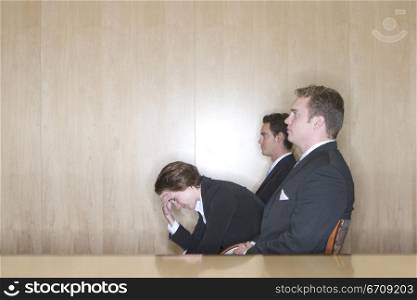 Business woman is stress as she holds her hand to her head while two other business men sit in their chairs