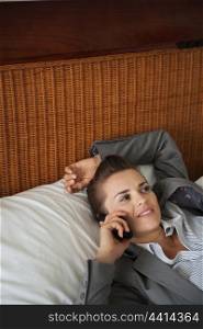 Business woman laying on bed in hotel room and talking cell phone