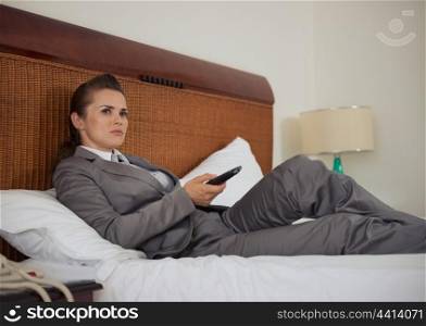 Business woman laying on bed in hotel room and watching tv