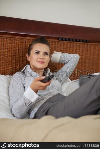 Business woman laying on bed in hotel room and watching tv