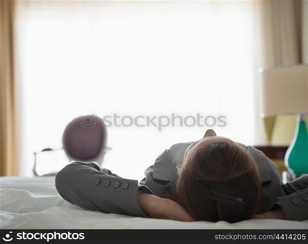 Business woman laying on bed in hotel room. rear view