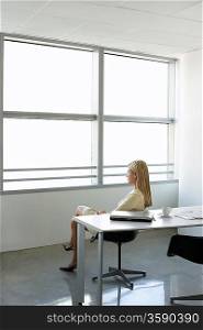 Business woman looking through window sitting in office