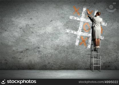 Business woman playing tictactoe. Businesswoman playing tictactoe on wall standing on ladder
