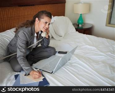 Business woman sitting on bed in hotel room and talking phone