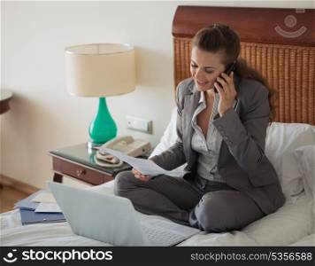 Business woman sitting on bed in hotel room and working