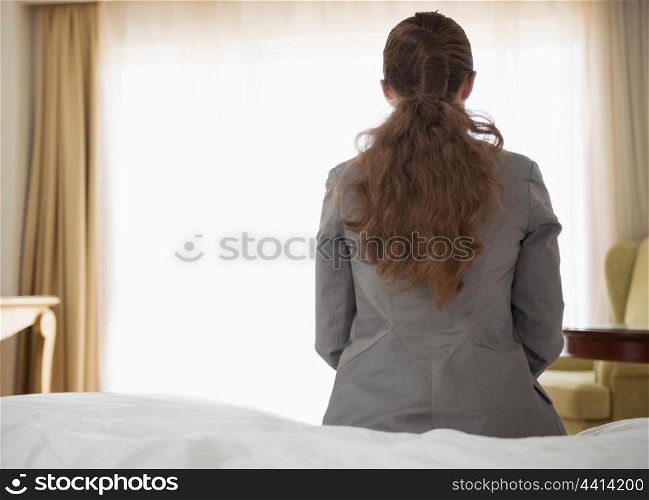 Business woman sitting on bed in hotel room. rear view