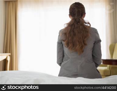 Business woman sitting on bed in hotel room. rear view
