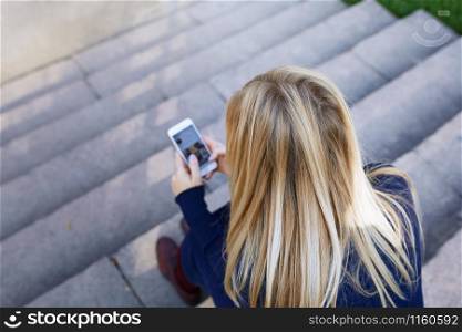 Business woman sitting on city stair steps and holding smartphone