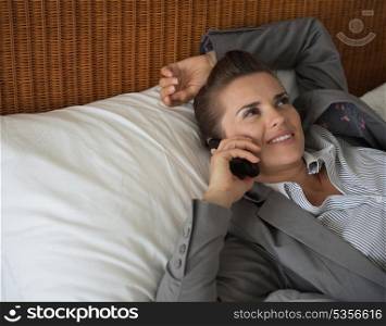 Business woman talking cell phone on bed in hotel room