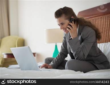 Business woman talking mobile phone and working on laptop in hotel room
