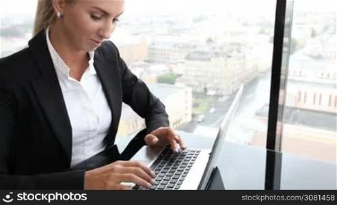 Business woman typing on laptop sitting by the window in office