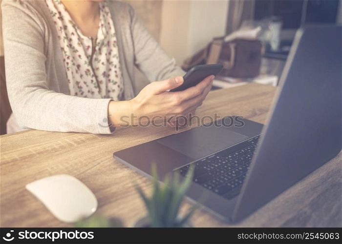 Business woman using laptop computer do online activity and holding phone on wood table.