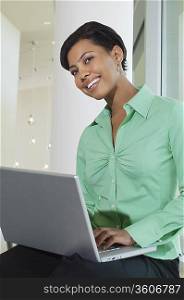 Business woman using laptop sitting on window ledge, low angle view