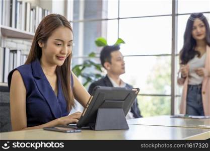 Business woman using modern digital tablet while coworker interacting in the background in the office , Teamwork meeting and partnership concept.