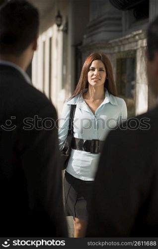 Business woman walking towards businessmen, outdoors