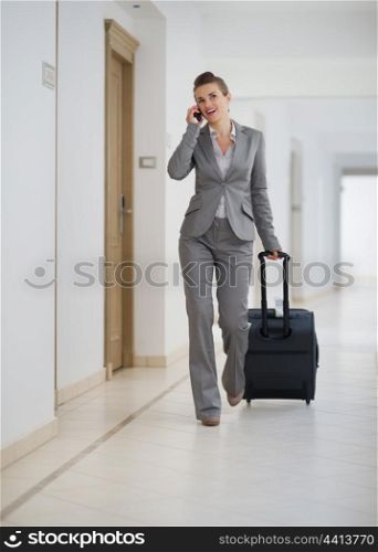 Business woman walking with bag on wheels and talking mobile phone