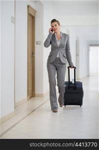 Business woman walking with bag on wheels and talking mobile phone