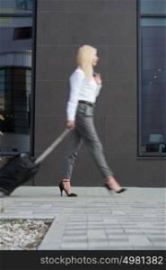 Business woman walking with suitcase near modern office building or hotel