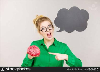 Business woman wearing green jacket and eyeglasses being rude and mad solution holding fake brain, black thinking or speech bubble next to her.. Business woman intensive thinking holding brain
